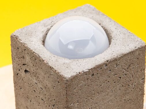 Lampa z betonu na tle żółtej ściany.