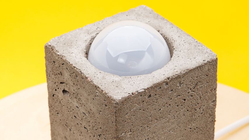 Lampa z betonu na tle żółtej ściany.